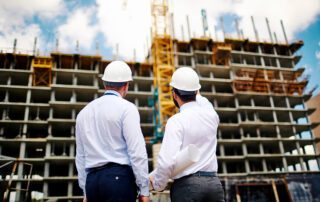 two contractors achitects looking up at partially built high-rise on construction site - construction contracts in compliance concept